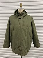 Front view of vintage olive green quilted winter work coat with hood, zip and snap button closure, and two large front pockets.