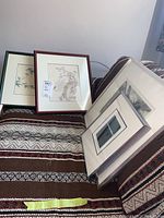 Four framed prints displayed on a patterned blanket showing variety of frames and matting.