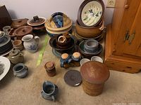 Overview of the collection showing multiple pottery bowls, lids, jugs, salt and pepper shakers on carpeted floor near wooden cabinet.