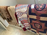 Multiple blankets and quilted runner displayed hanging, showing different materials and patterns.