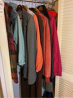 Nine coats and jackets hanging on rack showing various colors and styles including plaid, grey, orange, red, and green jackets.