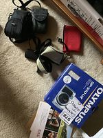 Photo of Olympus SP-510 UZ camera box, two mini cameras each in protective cases, and some camera accessories including manuals and straps.
