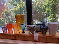 Nine glass vases arranged on a window sill showing color, size, and variety.