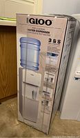 Boxed Igloo water dispenser showing front side of packaging with branding and main features listed.
