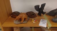 Top view of the lot showing two carved wood masks, a wood bear figure, a black stone bird figurine, and a small beadwork bird pin on a wooden shelf.
