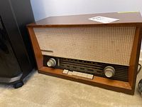 Front side of vintage Nordmende radio showing wooden case, woven fabric speaker grill, tuning dial, and push buttons.