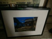 Framed photograph showing a building at night with illuminated signs and architectural details.