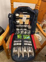 Full view of picnic backpack opened, showing cutlery, plates, glasses, salt and pepper shakers, cheese board, corkscrew, and blanket