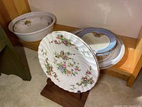 Porcelain dishes comprising Staffordshire pagoda plates, Country Garden platter, and two bowls on wooden shelf.