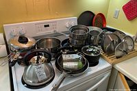 Wide photo showing kettles, saucepans, frying pans, lids, and rack arranged on stove and countertop.