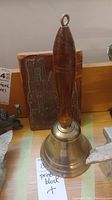 Photo of the brass bell with wooden handle and printing block behind it, showing relative size and materials.