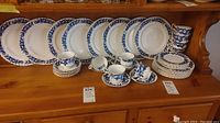 Full display of eight dinner plates, eight salad plates, six bread plates, eight saucers with teacups arranged on wooden shelf