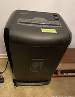 Front view of black Staples paper shredder showing controls and shredder slot on top with sticky label.