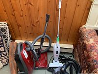 Red Panasonic BareFloor MC-CG902 canister vacuum with hose and metal wand next to white Bissell Featherweight stick vacuum.
