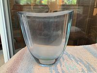 Front view of the clear glass vase showing its curved asymmetrical shape and transparency on a textured cloth.