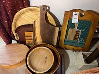 Photo showing several woodware items: round wood bowls, cutting boards with wood tones, and a painted wood wall coat hanger with heart cutout and hooks.