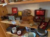 Shelf with multiple decorative boxes including wooden boxes with varied decorative lids, metal and stone trinkets, and small ceramic bowls and cups beneath.