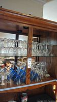 Various clear and blue base glassware including wine glasses and martini glasses on wooden shelves.