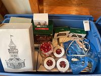 Boxed holiday village house and several sets of red candy cane string lights on blue plastic bin.