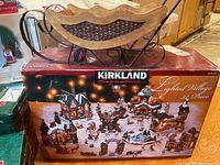 Box of Kirkland Signature Lighted Christmas Village Set, showing 23 pieces and festive design.