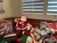 Photo showing plush Santa Claus doll, reindeer plush, holiday textile items including placemats, and boxed Santa suit.