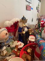 Photo showing Christmas nutcracker figurine, snowman plush, Santa stuffed figures, and a red and white fur trimmed stocking hanging behind them.