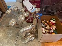 Silverplated reindeer candle holder with five candle cups shown from an angle, placed next to a box of Christmas ornaments on a tiled floor.