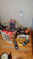 Photo of several loose and boxed NASCAR die-cast collectible cars with visible sponsor logos and car numbers arranged on floor near wall.