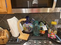 Overview photo of all items: ceramic cookie jar, blue glass jar, colorful ceramic bird vase, glass juice pitcher with yellow lid, wooden paper towel holder, wooden knife block with knives.