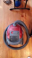 Top-down photo of red Electrolux Harmony bagless canister vacuum cleaner with grey hose on wooden floor.