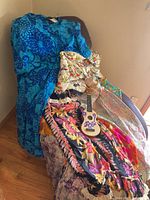 Assortment of four Hawaiian style dresses and a small decorated toy ukulele displayed on a chair and floor showing colors and patterns.