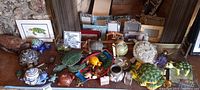 Photo of an assortment of turtle-themed home decor items including multiple ceramic and resin turtle figurines, a turtle-shaped clock, and numerous picture frames in the background.