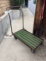 Full view of metal dolly showing handle, rusted frame, and four wheels on concrete surface