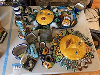 Full view of lot showing colorful hand-painted Mexican pottery items including two large sun face plates, candle holders, planters, and trays arranged on a table.