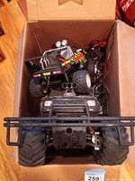 Top view of two remote control trucks inside a box, showing the smaller Eliminator and larger Black Thunder models with controllers and wiring visible.