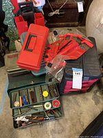 Photo showing multiple tool boxes stacked and assorted hand tools around them including a red toolbox, a small blue-green toolbox, and various items.