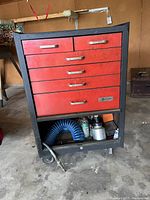 Front view of the rolling tool chest showing closed red drawers and open bottom shelf with tools and hose.
