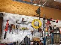 Tools hanging on pegboard including saws, clamps, screwdrivers, a yellow fish tape reel, and storage drawers.