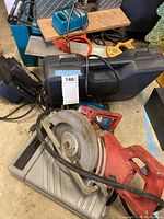 Photo of a red Milwaukee circular saw, power chargers, and black carrying cases piled together on a floor.