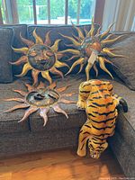 Three metal sun wall hangings placed on a gray couch with the paper mache tiger figurine.