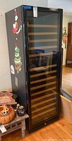 Front exterior view of closed black wine cooler with glass door and holiday stickers on side
