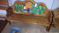 Full view of wooden bench with colorful painted desert scene on backrest showing cacti and a seated figure in a sombrero.