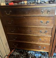 Front view of one wooden antique dresser showing five drawers with vintage brass handles and visible scratches.