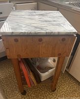 Full view of butcher block kitchen prep table with white marble top, showing wood grain detail and caster wheels.