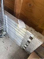 Folded metal scaffolding stacked on the ground, showing the metal tubular structure and hinge connections.