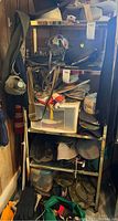 Metal shelving unit packed with various hats including camouflage, visors, and caps, winter gloves and scarves visible in lower sections, some hats stacked on plastic drawers.