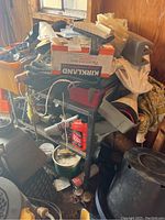 Metal cart loaded with various hand tools, hardware and supplies in a shed with wooden walls.