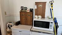 Microwave, two wooden spice cabinets, mugs, and ceramic water jug on stand arranged on counter