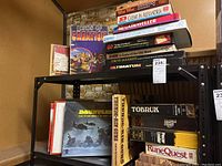 Full shelf view showing multiple vintage role playing and tabletop games in a black shelf with visible titles like Lords of Creation, Caesar in Alexandria, and The Caraveller.