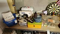 Overview of two sewing machines and various sewing supplies on table including thread, bobbins, and storage boxes